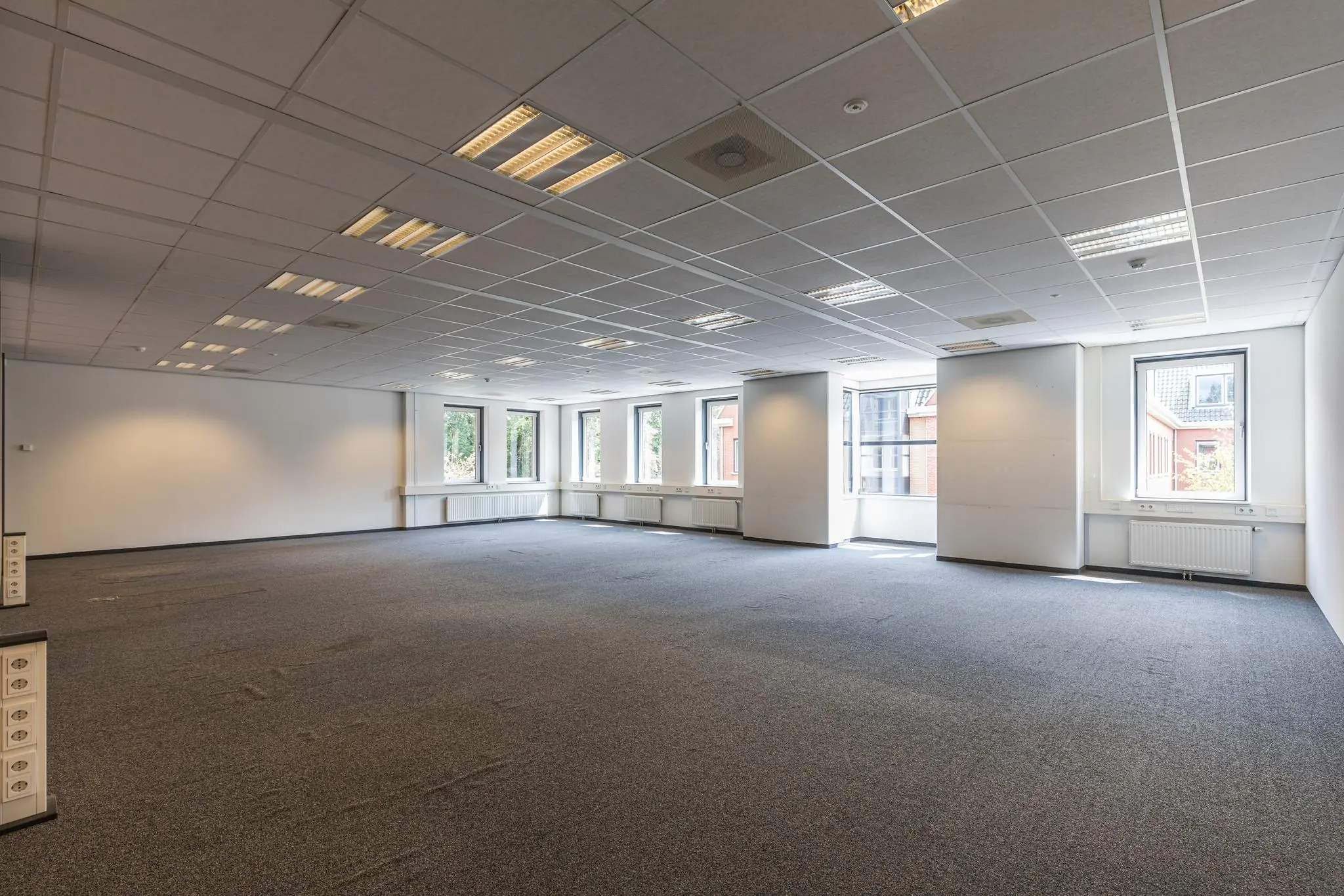 Leeg kantoorpand aan de Laan Blasse van Oud-Alblas met tapijt, systeemplafond en meerdere ramen met uitzicht op naastgelegen gebouwen.